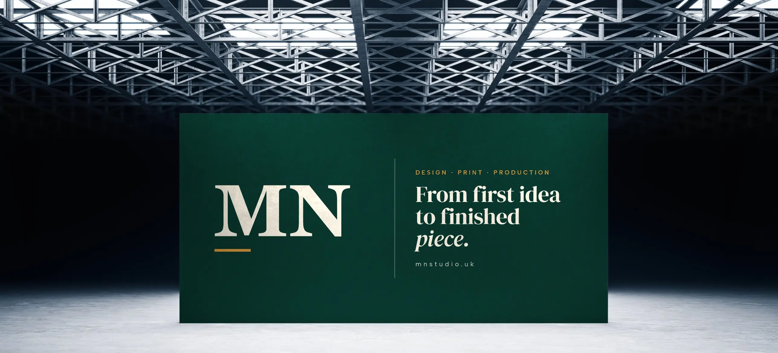 A large green MN Studio backdrop reading “From first idea to finished piece” beneath a steel-truss ceiling