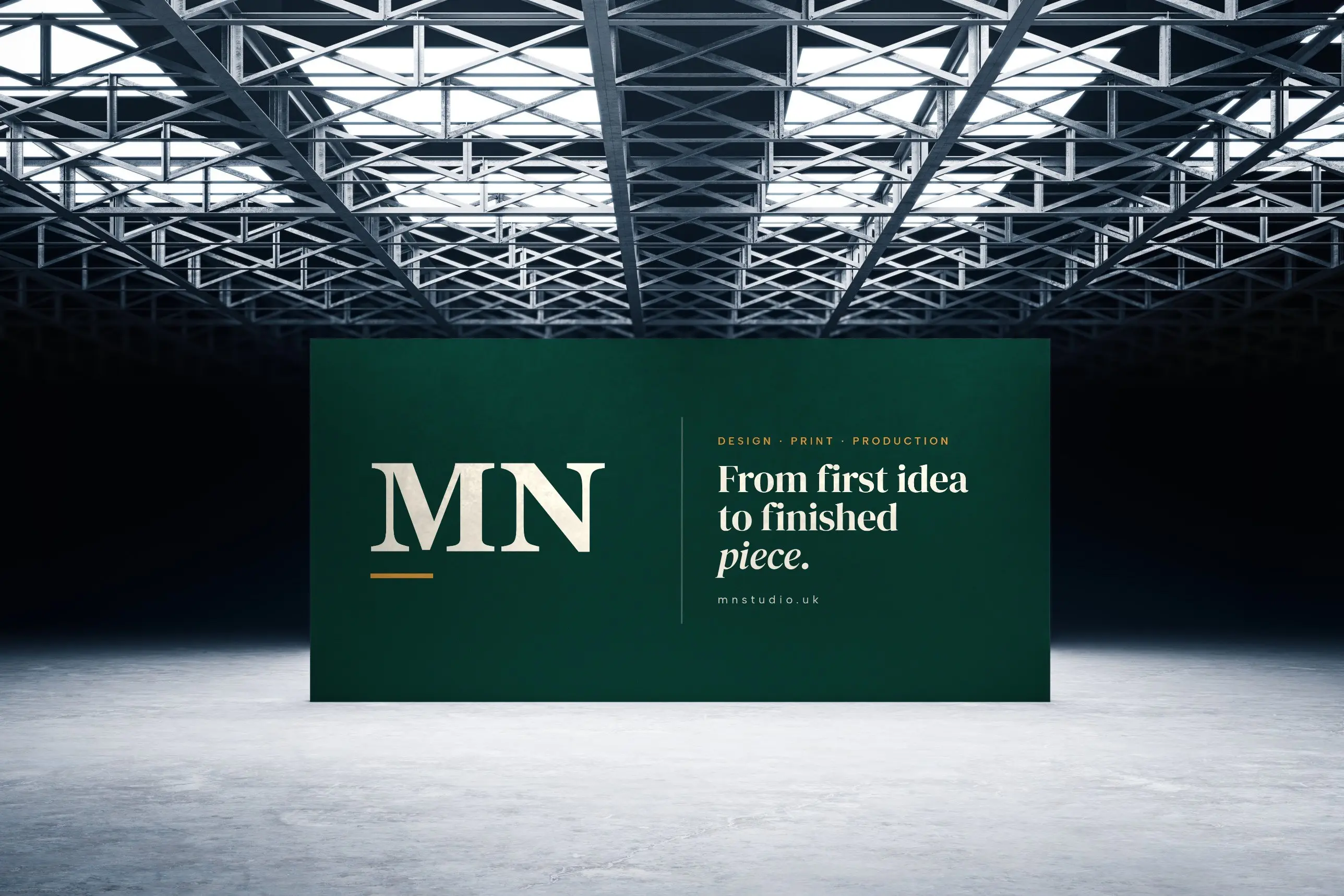 A large green MN Studio backdrop reading “From first idea to finished piece” beneath a steel-truss ceiling
