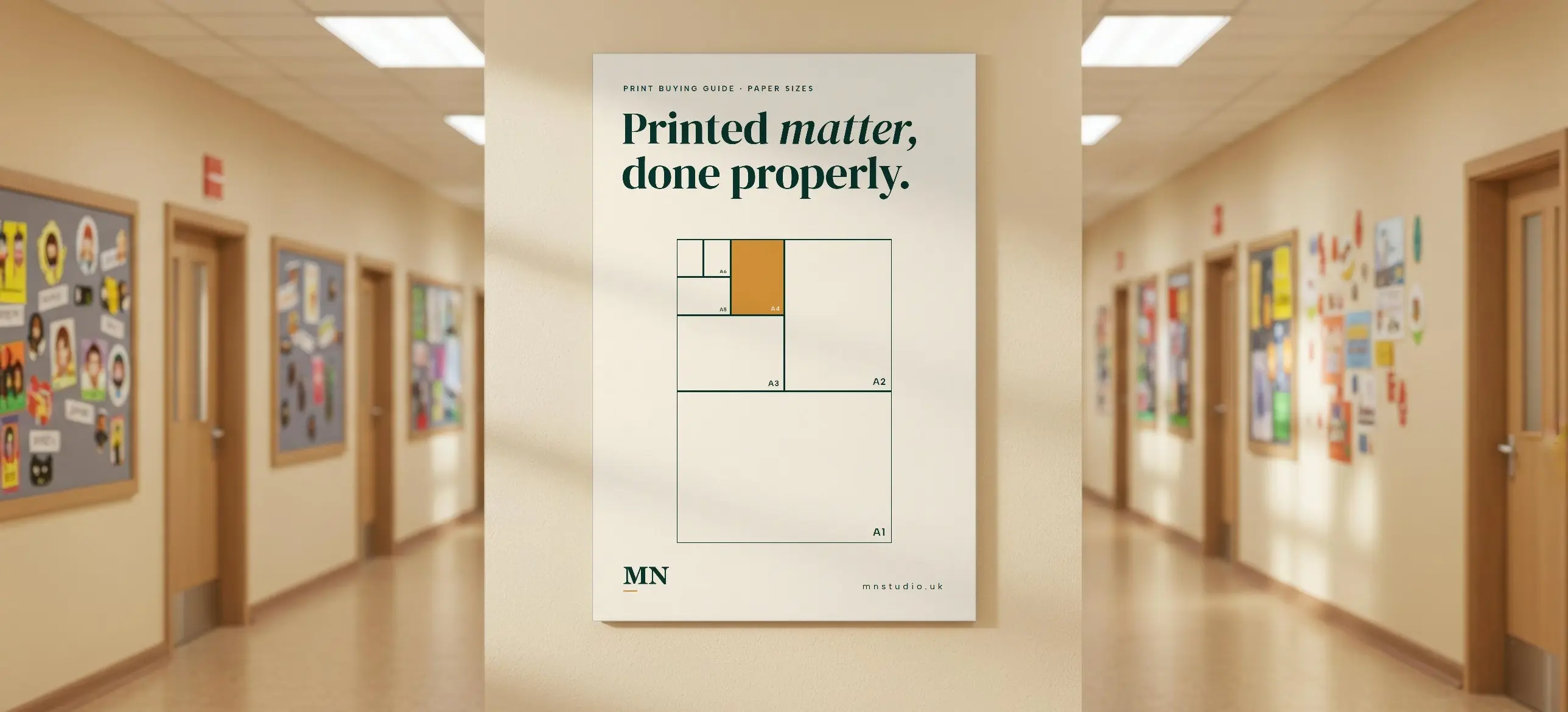 A cream MN Studio poster showing A-series paper sizes, hung on a corridor wall