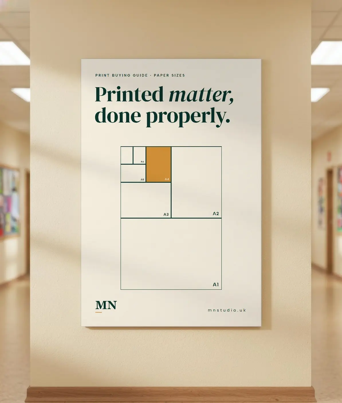 A cream MN Studio poster showing A-series paper sizes, hung on a corridor wall