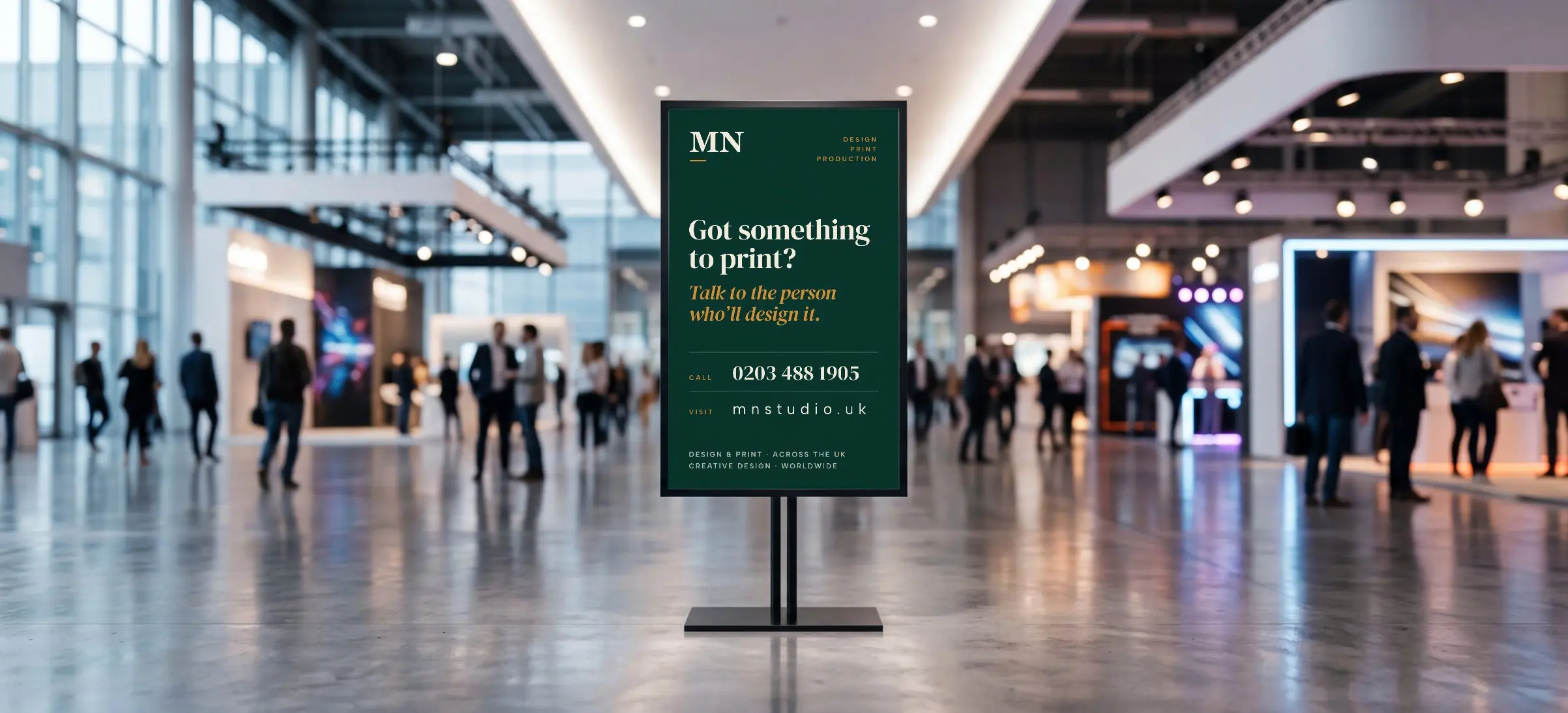 An MN Studio poster on a freestanding display stand in a busy exhibition hall